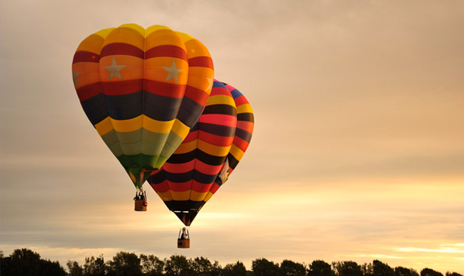 2 multicoloured hot air balloons with a sunset